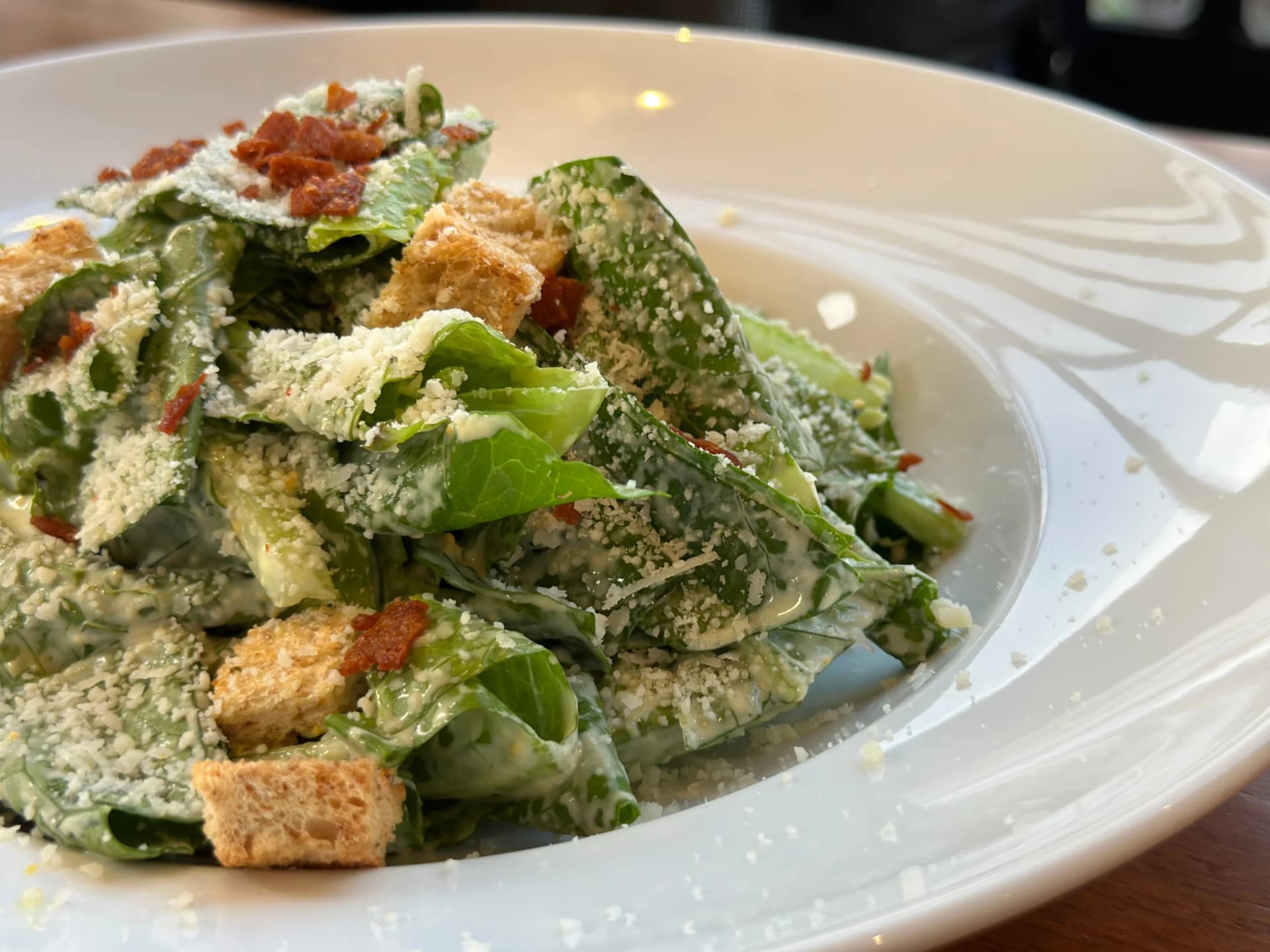 Caesar salad with romaine lettuce, croutons, bacon bits, and grated cheese on a white plate.