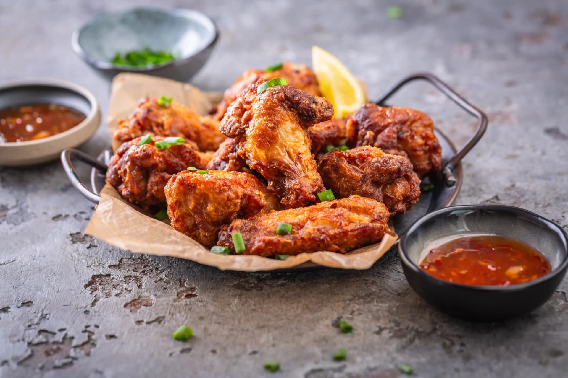 Crispy fried chicken wings garnished with green onions, served with dipping sauce and lemon wedge on a rustic platter.